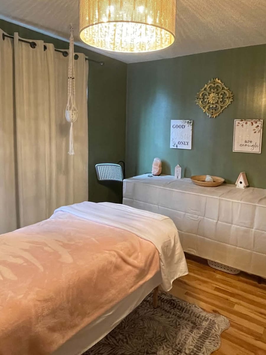 Christine's treatment room: sage-green walls, a warm woven pendant light and a massage table under a soft pink blanket
